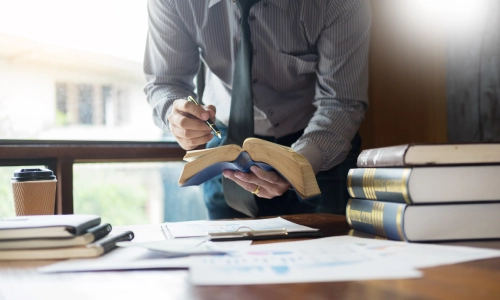 A dog bite lawyer serving Arizona is standing and leaning forward while reading a book in his hands and pointing to it with a pen