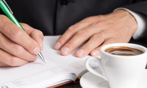 An Arizona Lyft accident lawyer writing notes at his desk, with a cup of black coffee in front of him.