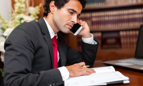 An Arizona motorcycle accident lawyer is speaking on the phone while reviewing notes written in his notebook.