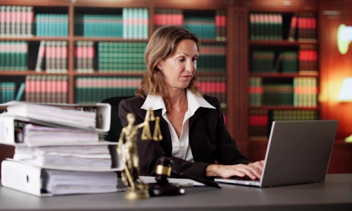 An Arizona negligence lawyer typing on her laptop, with a gavel hammer, a lady justice statue, and a stack of legal documents on the desk.