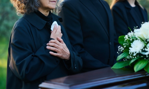 A grieving woman standing in front of the coffin of her loved one, considering seeking assistance from a California wrongful death lawyer.