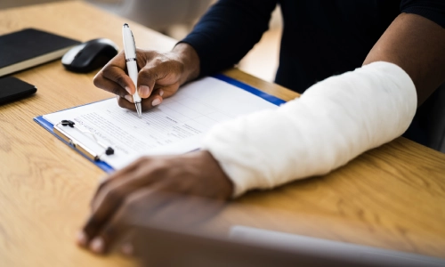 A victim of an accident with an arm in a cast filling up papers for a claim.