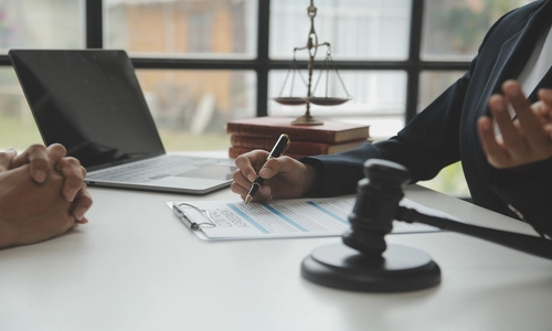 A Nogales negligence lawyer discussing a case with a client while taking notes, with a gavel beside her on the table.