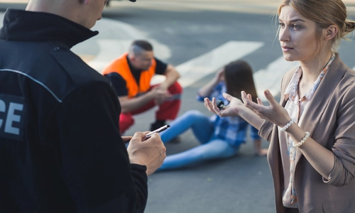 A woman discussing the accident with the police, while another woman lies on the pedestrian lane in the background, being assisted by a rescue personnel.