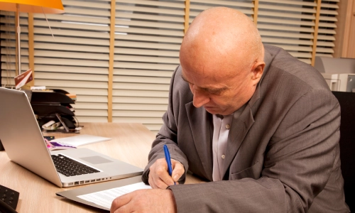 A Nogales wrongful death lawyer writing notes in front of his laptop and office telephone.
