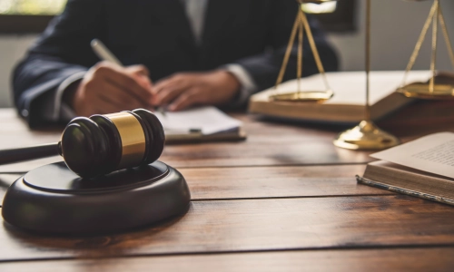 A Riverside Boat Accident Lawyer writing on files inside a clipboard on top of an office desk with a hammer and gavel in the foreground