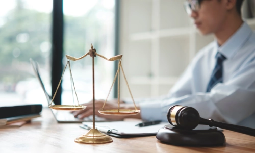 An Asian lyft accident lawyer typing on a laptop in a Riverside law office with scales of justice in closer view