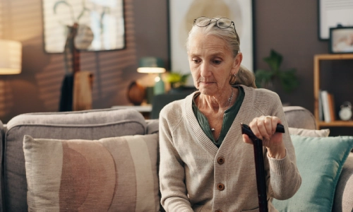 A photo of a sad elderly woman sitting on a couch, reflecting thoughtfully.
