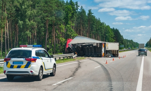 A photo of an overturned truck on the road with a police car investigating the crash.