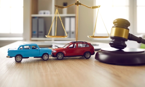 A photo of two miniature cars, a gavel, and a scale of justice on a table.