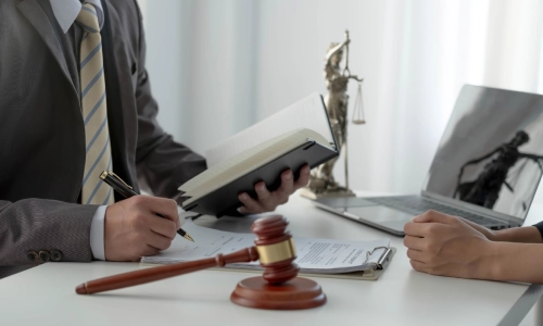 A photo of a Riverside workers’ compensation lawyer writing notes while discussing a case with a client, with a gavel on the table beside him