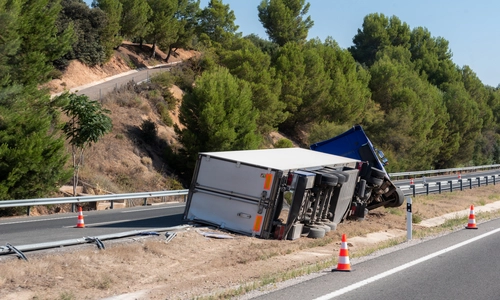 A photo of an overturned truck at a highway exit, causing damage to road hardware.