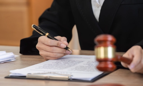 A Construction Accident Lawyer is writing on a document while holding a mallet in their left hand and sitting inside a Tempe Law office