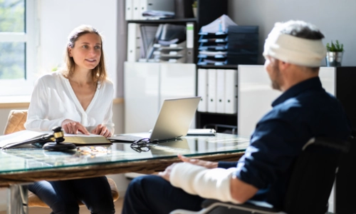 A Tempe personal injury lawyer discussing legal matters with a client, referring to a book, with a laptop in front of her.