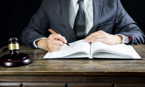 A motorcycle accident lawyer sits inside a Tucson law office while writing notes on an open book while a hammer and gavel lie on the table