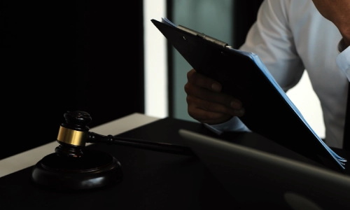 A Tucson Truck Accident Lawyer thinks while sitting in his office while placing one hand on their chin and reading a document on a black clipboard