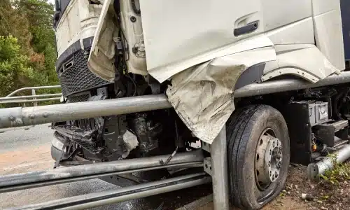 A commercial truck crashing into a metal barrier on the road.