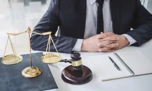 A bus accident lawyer serving the Bronx leans forward on an office desk while reading the contents of a notebook lying beside a hammer and gavel and balance scales