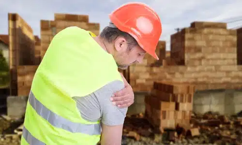 A construction worker holding his shoulder in pain from a construction site accident.