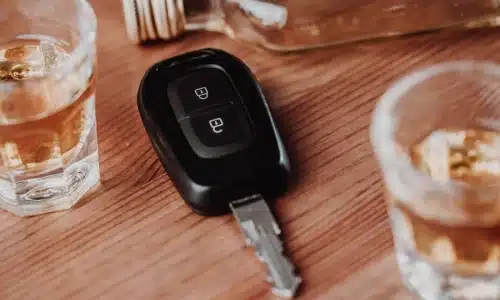 A car key lying on a wooden table next to bottles and shot glasses of alcohol.
