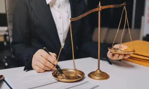 A car accident lawyer serving Long Island is pushing down on one side of a balance scale using a pen while they sit inside a law ofiice