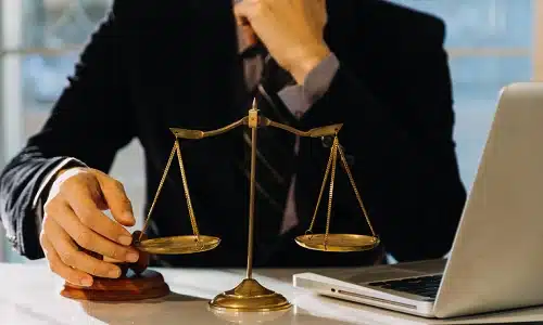 A rideshare accident lawyer serving Long Island is reading documents on his laptop while sitting at a cluttered desk inside a law office