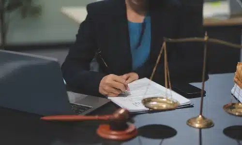 A slip and fall accident lawyer serving Long Island sits while signing legal documents attached to a clipboard kying on an office desk