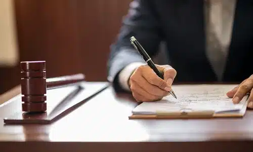 An electric scooter accident lawyer serving Manhattan writes case notes at a desk with a wooden gavel hammer nearby.