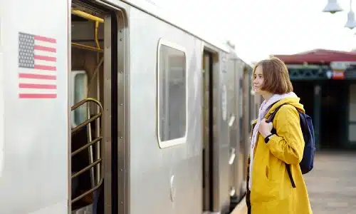 A woman in a yellow coat at a train station getting ready to board a train.