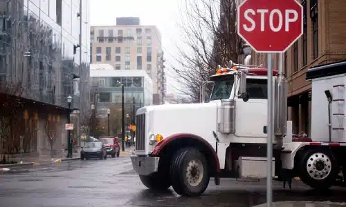 A white semi truck pulling a trailer on a road stopped behind a stop sign.