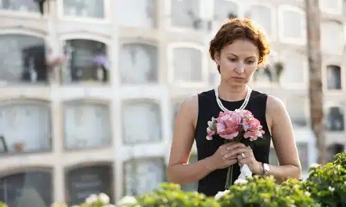 A woman in a black dress holding a bouquet while mourning at the funeral of a wrongful death victim.