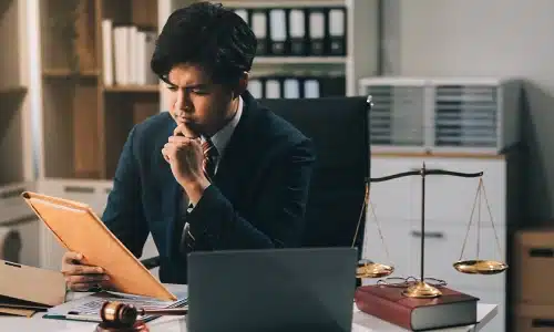 A defective product lawyer serving Queens reviews legal documents at a desk with a laptop, a scale of justice, and a wooden gavel.